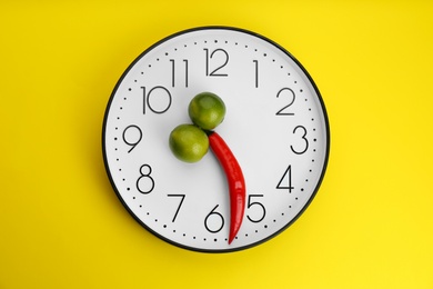 Photo of Clock with pepper and limes on yellow background, top view. Potency problem concept