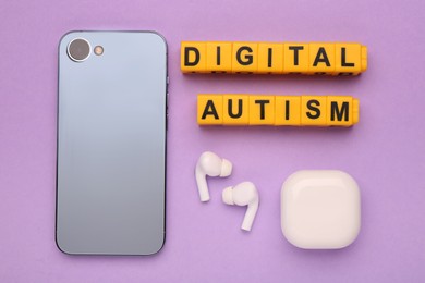 Photo of Phrase Digital Autism made of yellow cubes, smartphone and earphones on violet background, flat lay. Addictive behavior