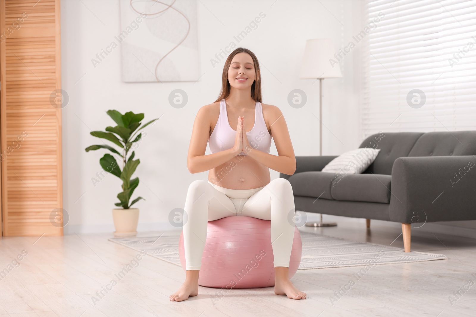 Photo of Pregnant woman meditating on fitness ball in room. Home yoga