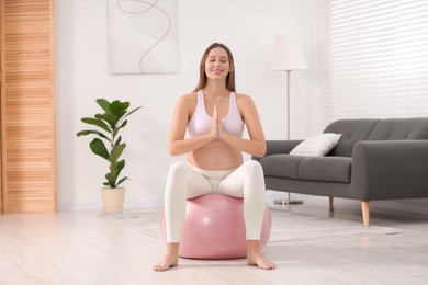 Pregnant woman meditating on fitness ball in room. Home yoga