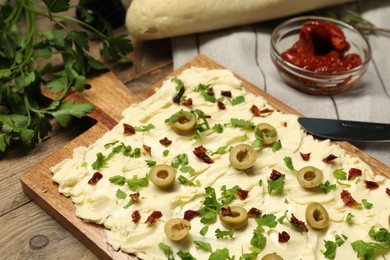 Photo of Fresh butter board with cut olives, sun-dried tomatoes and parsley on wooden table