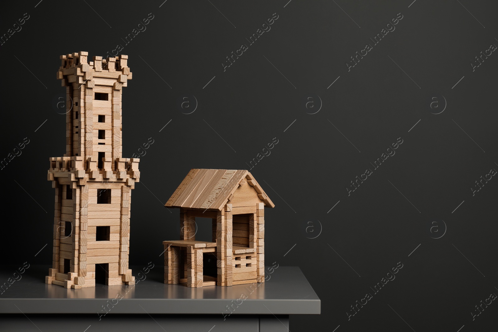 Photo of Wooden tower and house on table near dark grey wall, space for text. Children's toys