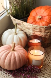 Wicker basket with beautiful heather flowers, pumpkins and burning candles near window indoors
