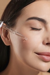 Photo of Beautiful young woman applying serum onto her face, closeup