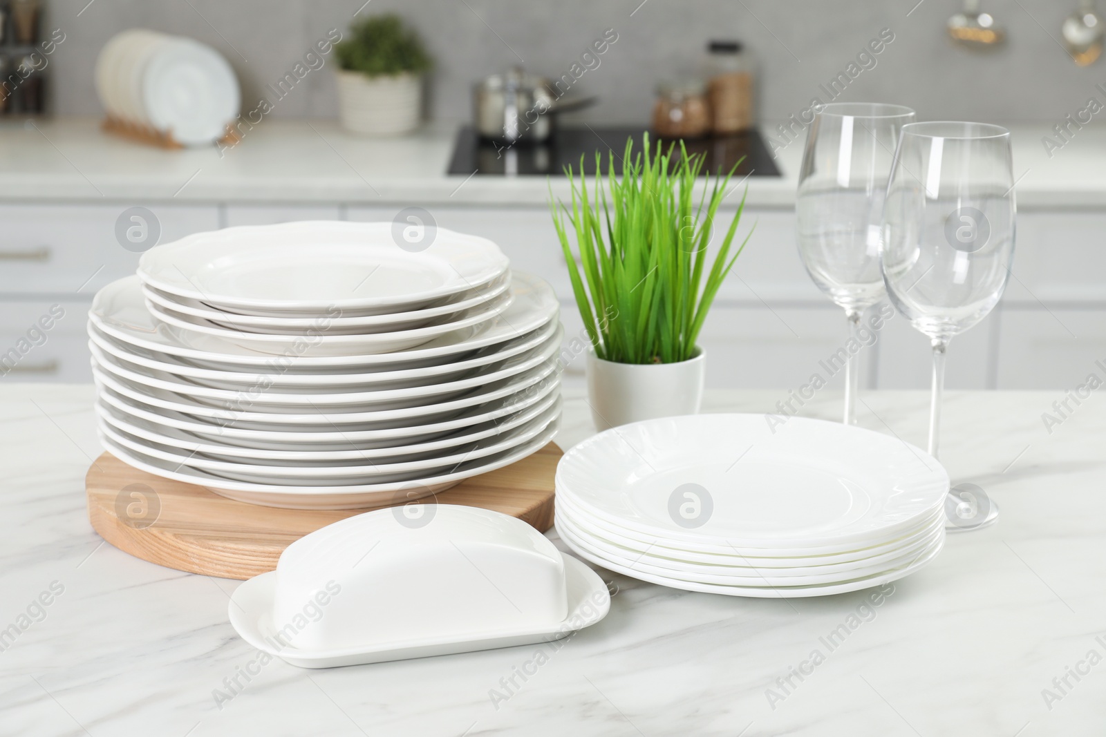 Photo of Clean plates, glasses, butter dish and floral decor on white marble table in kitchen