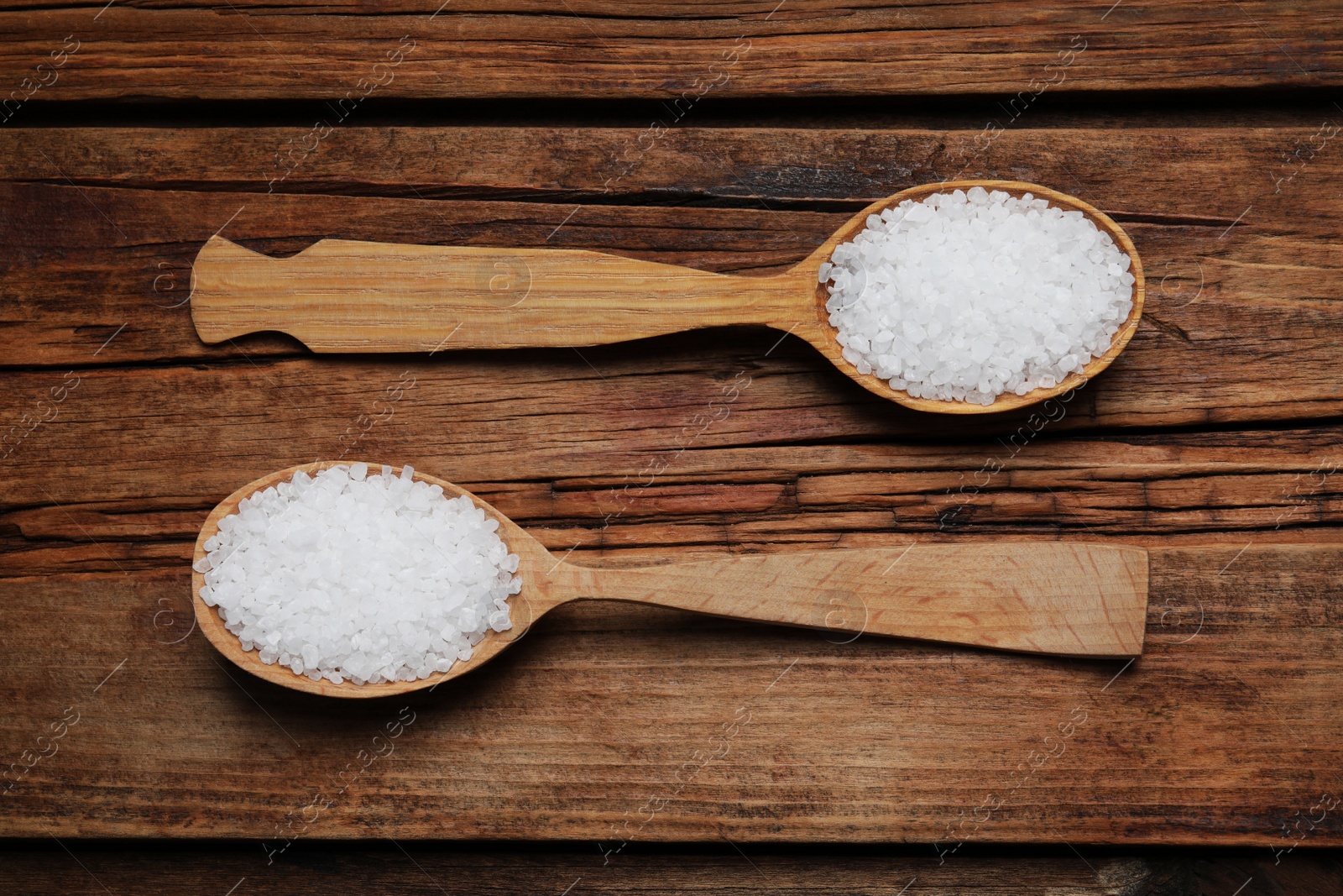 Photo of Spoons with natural sea salt on wooden table, flat lay
