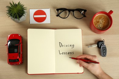 Photo of Woman with workbook for driving lessons and cup of coffee at white wooden table, top view. Passing license exam