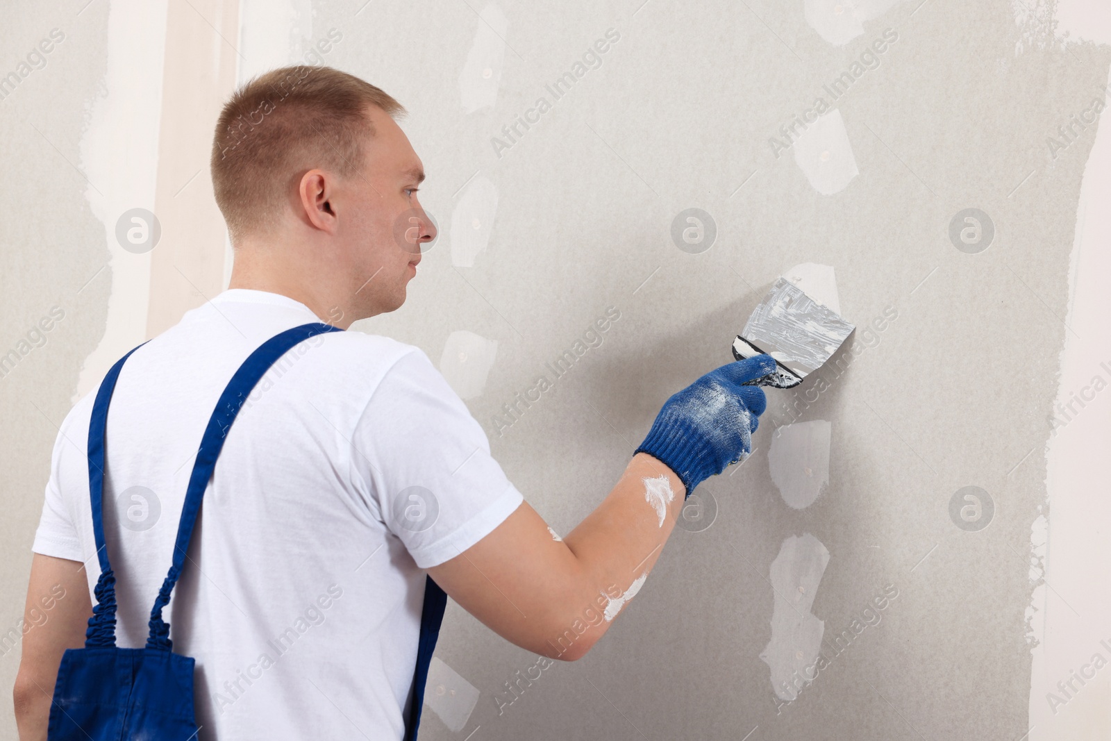 Photo of Man plastering wall with putty knife indoors. Home renovation