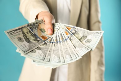Photo of Woman holding dollar banknotes on turquoise background, closeup. Money exchange concept