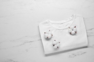 Photo of Fluffy cotton flowers and t-shirt on white marble background, top view. Space for text