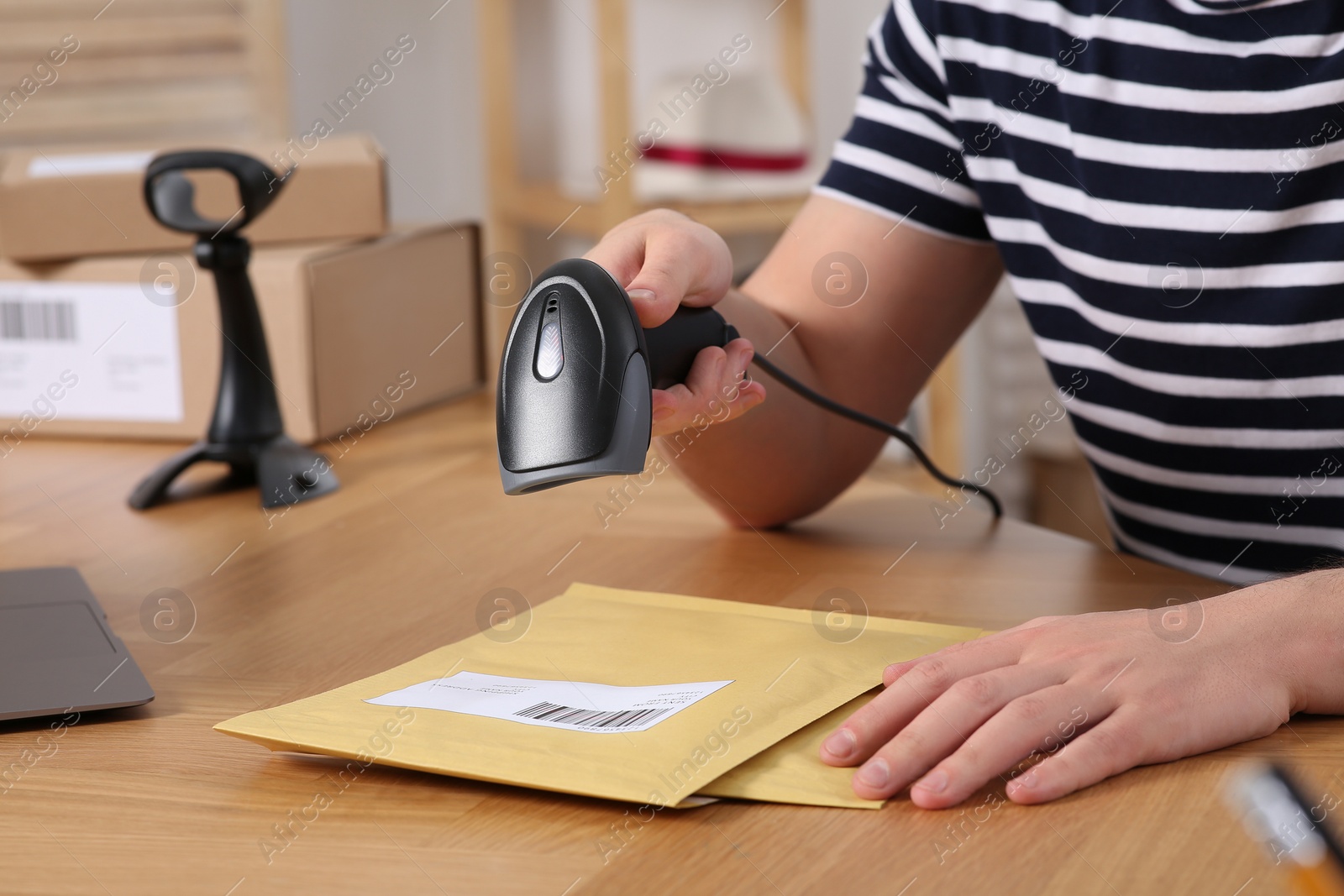 Photo of Seller with scanner reading parcel barcode at table in office, closeup. Online store