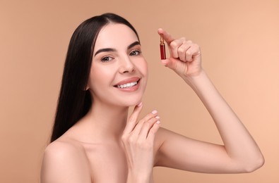 Beautiful young woman holding skincare ampoule on beige background