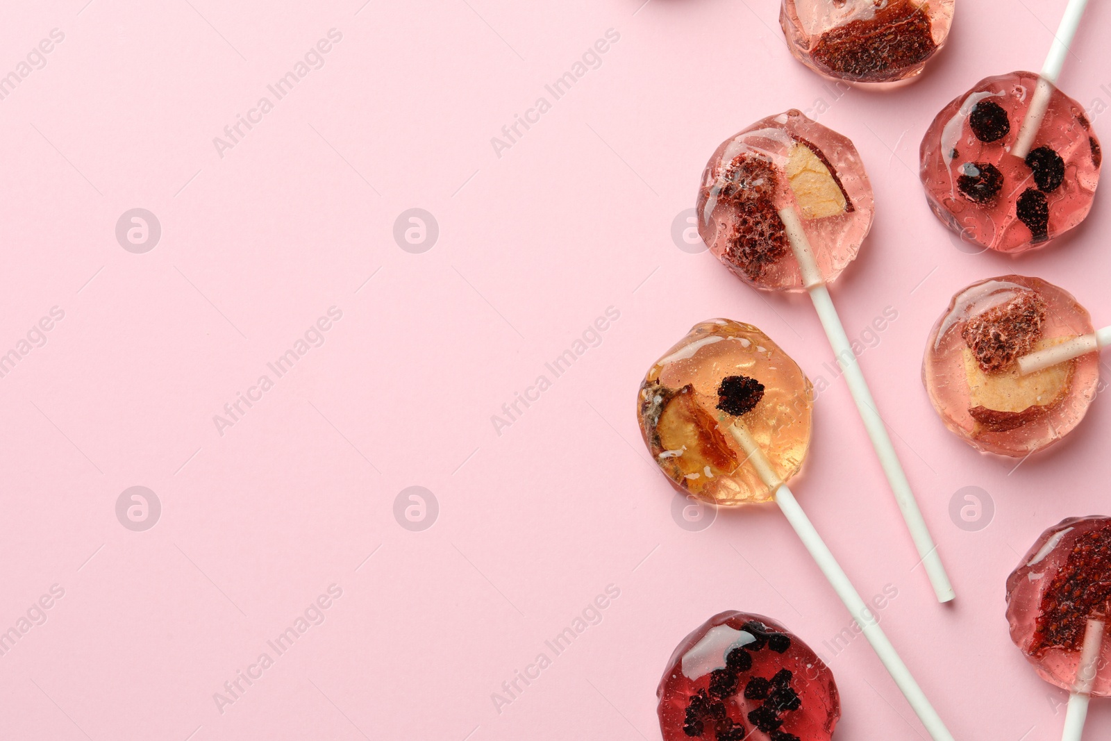 Photo of Sweet colorful lollipops with berries on pink background, flat lay. Space for text