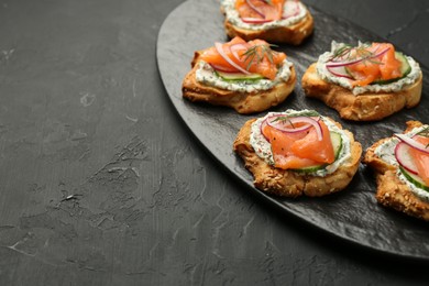 Photo of Tasty canapes with salmon, cucumber, radish and cream cheese on black table, space for text