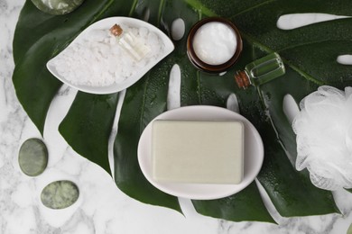 Flat lay composition with different spa products and tropical leaf on white marble table