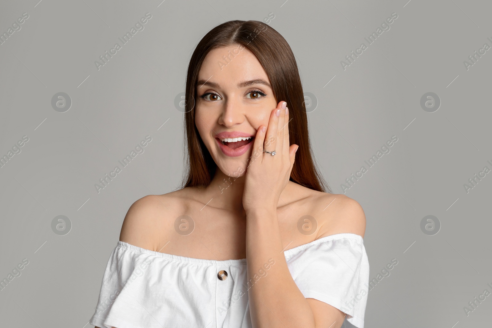 Photo of Emotional young woman wearing beautiful engagement ring on grey background