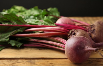 Bunch of fresh beets with leaves on wooden table against black background. Space for text