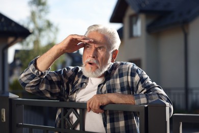 Photo of Concept of private life. Curious senior man spying on neighbours over fence outdoors