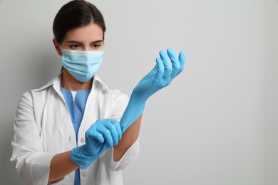 Photo of Doctor in protective mask putting on medical gloves against light grey background. Space for text