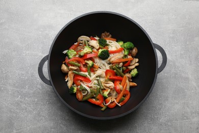 Photo of Stir fried noodles with mushrooms, chicken and vegetables in wok on light grey table, top view