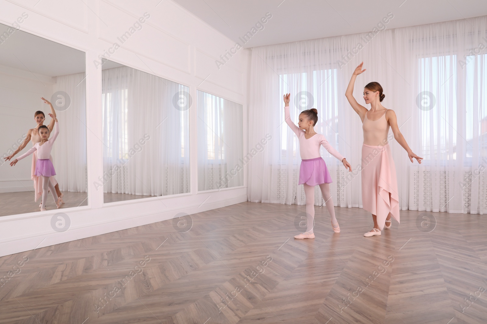 Photo of Little ballerina and her teacher practicing dance moves in studio