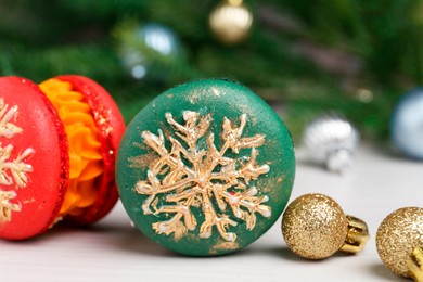 Photo of Different decorated Christmas macarons and festive decor on white table, closeup