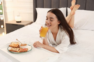 Photo of Happy young woman having breakfast on bed at home