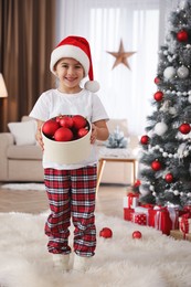 Cute little girl holding box with Christmas balls at home