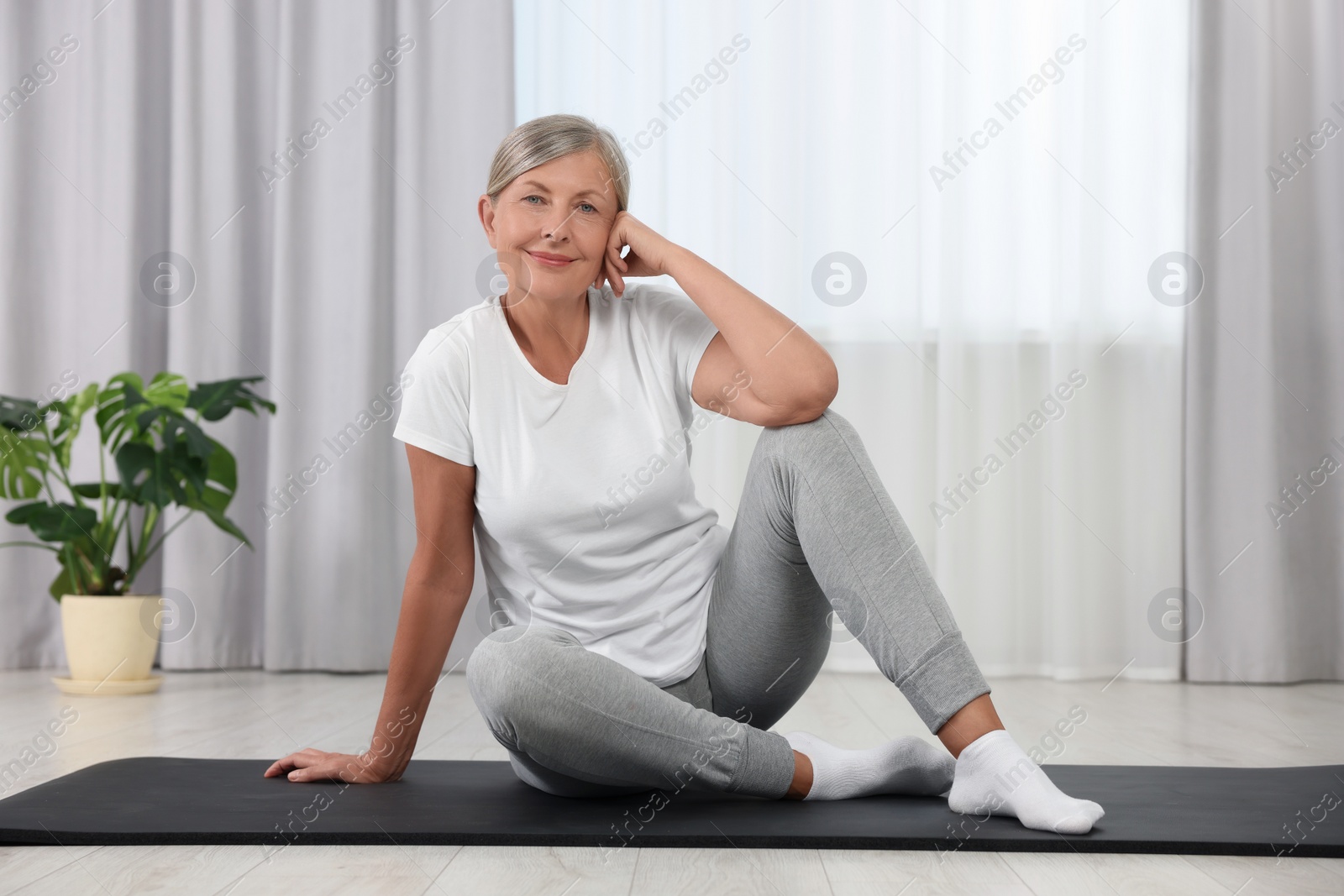 Photo of Happy senior woman sitting on mat at home. Yoga practice