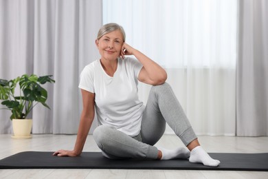 Happy senior woman sitting on mat at home. Yoga practice