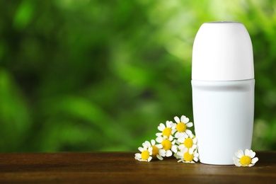 Photo of Natural roll-on deodorant with chamomile flowers on wooden table against blurred green background. Space for text