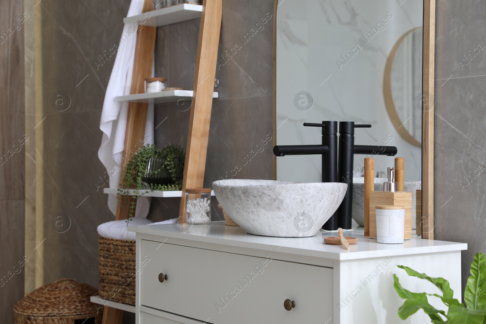 Photo of Stone vessel sink with faucet and toiletries on white countertop in bathroom