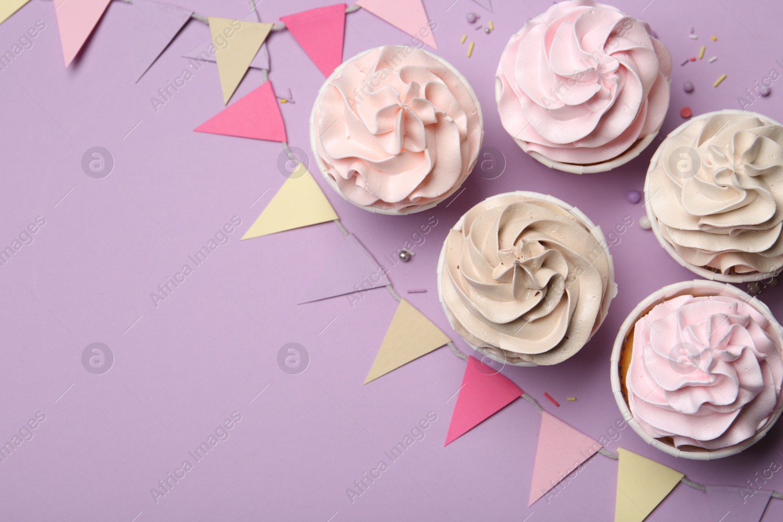 Photo of Delicious birthday cupcakes, sprinkles and bunting flags on violet background, flat lay. Space for text