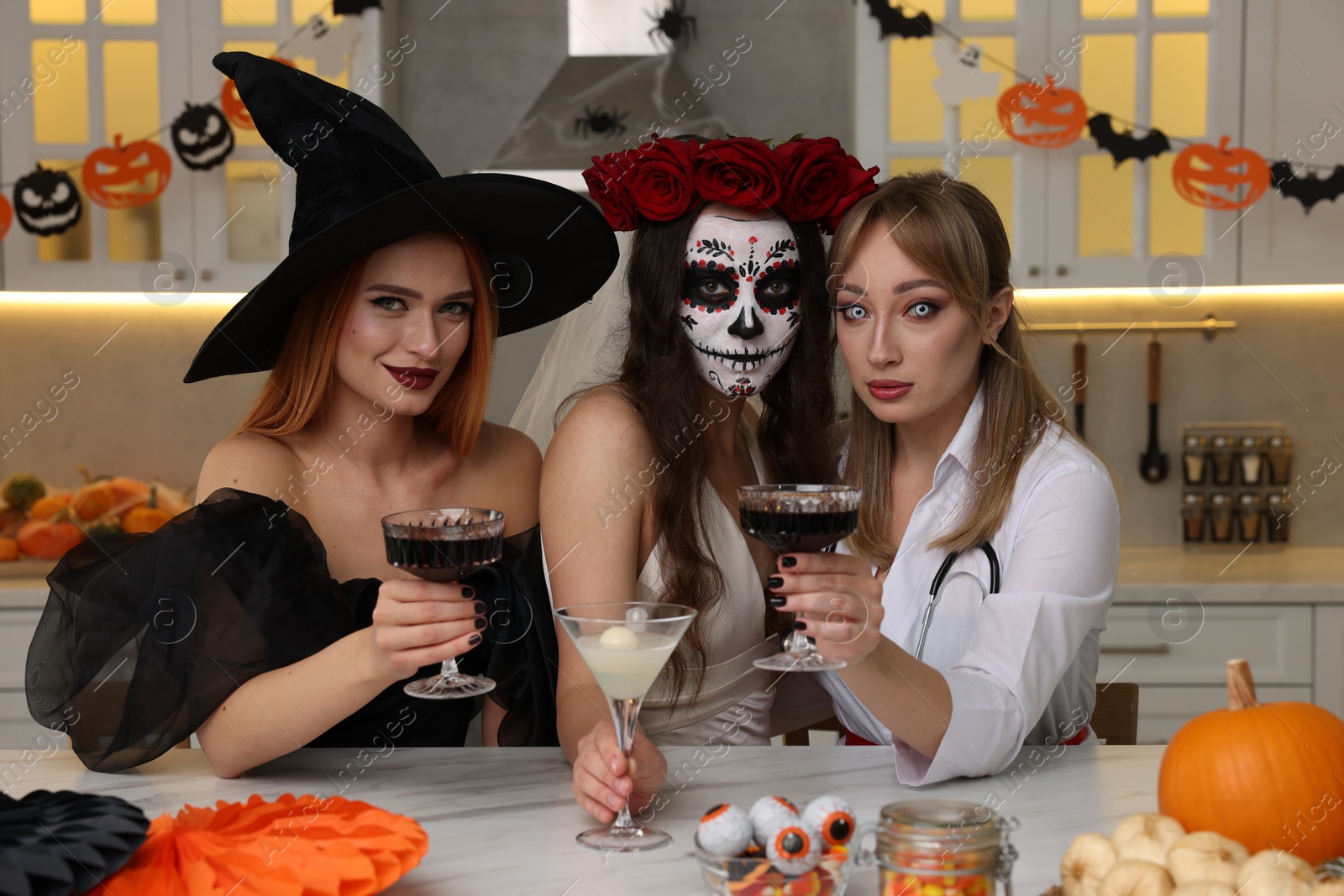 Photo of Group of women in scary costumes with cocktails celebrating Halloween indoors