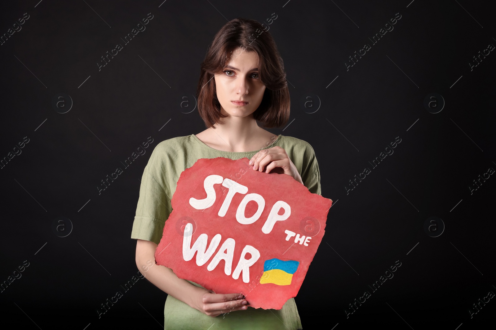 Photo of Sad woman holding poster with words Stop the War on black background