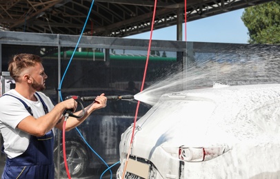 Young worker cleaning automobile with high pressure water jet at car wash