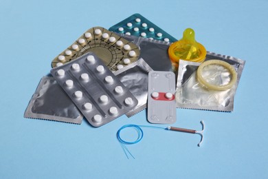Photo of Contraceptive pills, condoms and intrauterine device on light blue background. Different birth control methods