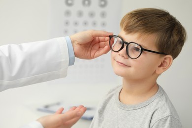 Photo of Vision testing. Ophthalmologist giving glasses to little boy indoors