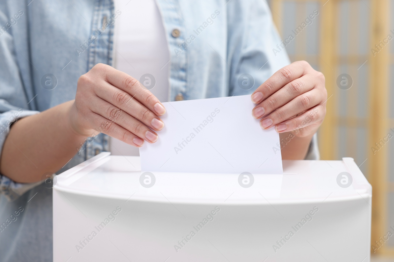 Photo of Woman putting her vote into ballot box on blurred background, closeup