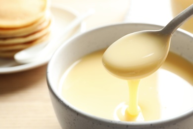 Spoon of pouring condensed milk over bowl on table, closeup with space for text. Dairy products