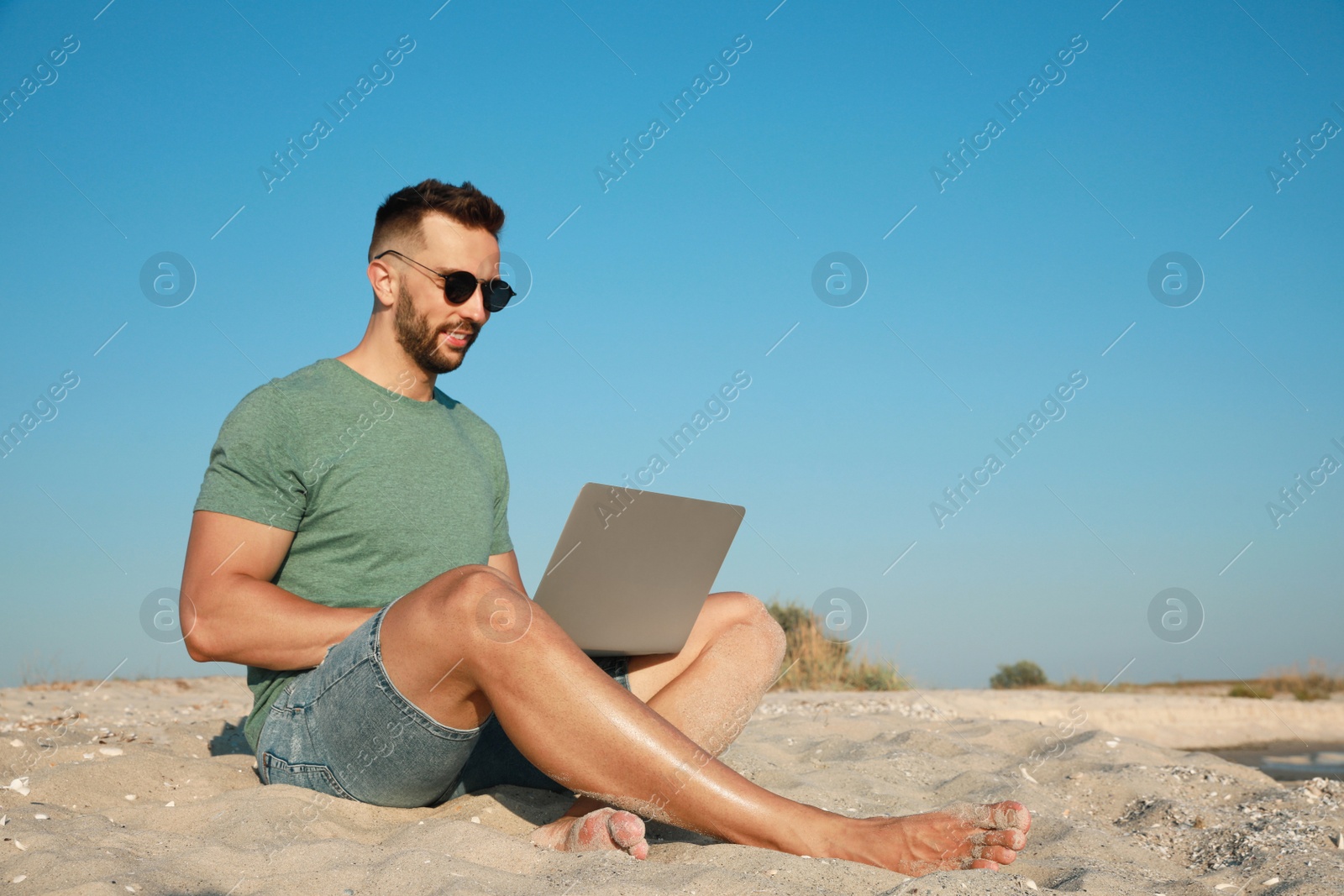 Photo of Man working with laptop on beach. Space for text