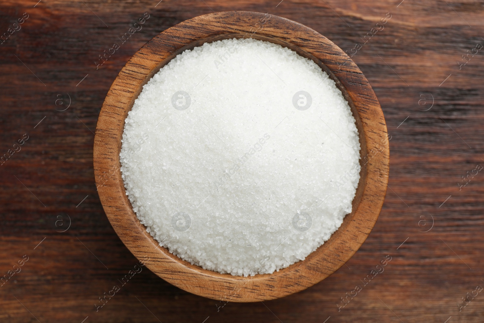 Photo of Granulated sugar in bowl on wooden table, top view