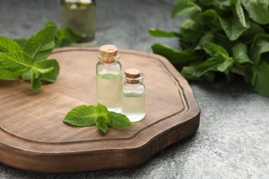Photo of Bottles of essential oil and mint on grey table