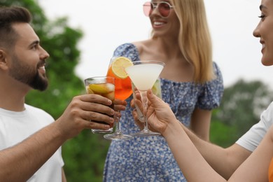Photo of Happy friends clinking glasses with cocktails outdoors, selective focus