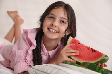 Photo of Cute little girl with watermelon on bed at home