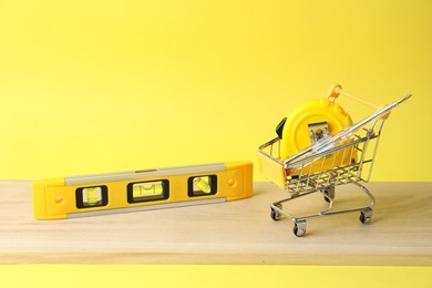 Photo of Small shopping cart and set of construction tools on yellow background