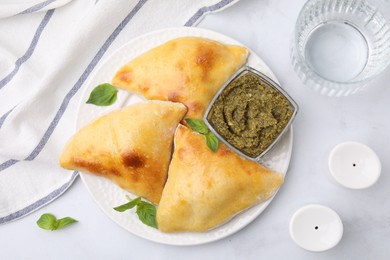 Photo of Delicious samosas with basil and pesto sauce on white marble table, flat lay