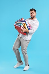 Photo of Stressful man with folders walking on light blue background