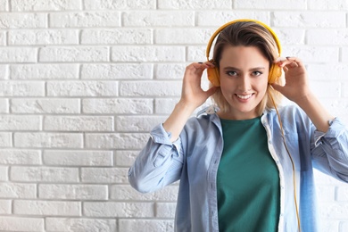 Photo of Portrait of beautiful woman listening to music with headphones near brick wall. Space for text