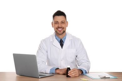 Professional pharmacist with syrup and laptop at table against white background